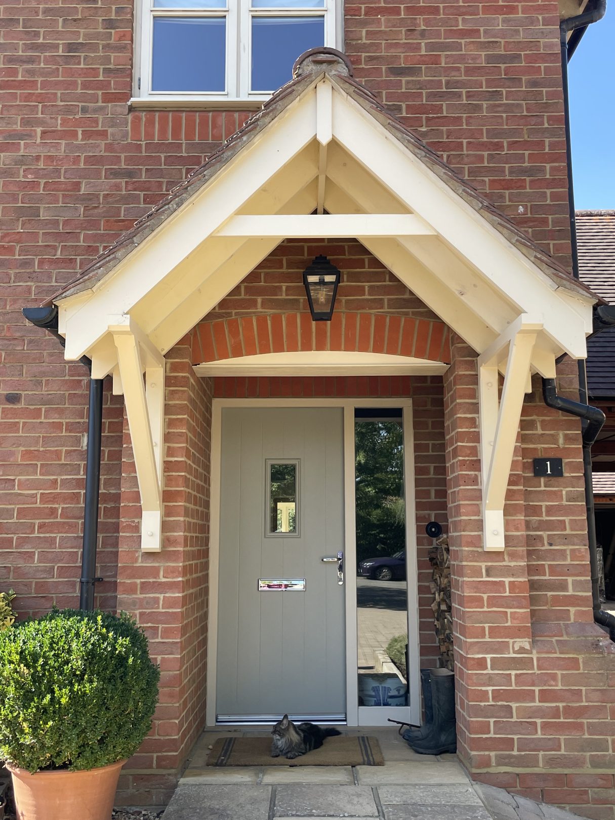 Brick house entrance with a cream timber porch canopy over a sage green front door