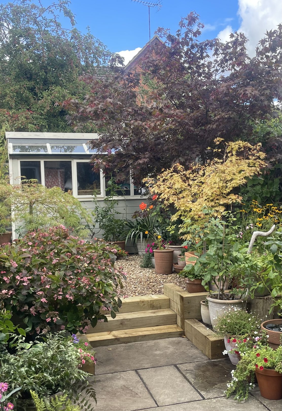 Timber sleeper steps and raised edging leading from a stone patio up to a gravel garden with a summerhouse