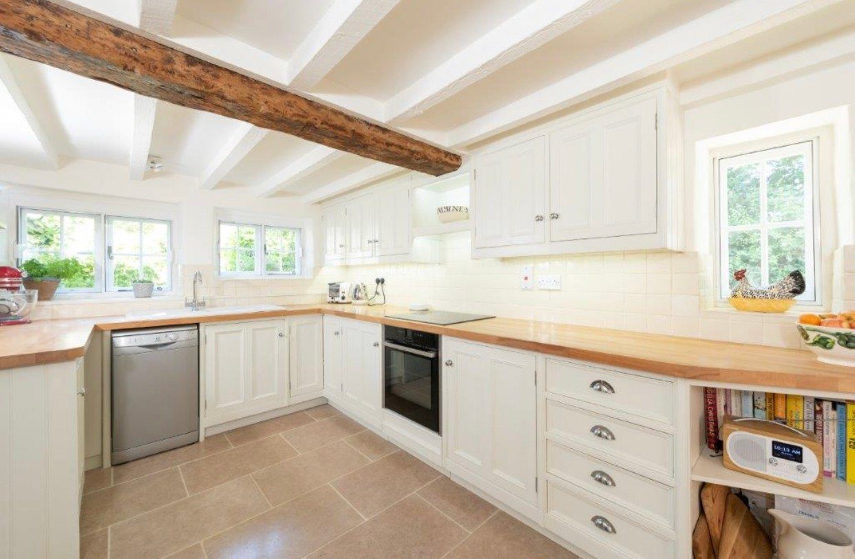 Bright country kitchen with cream painted cabinets, wooden worktops, stone floor tiles and exposed beams