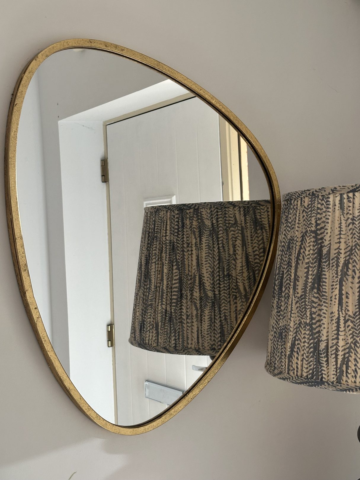 Curved gold-framed mirror hung on a hallway wall beside a patterned lampshade