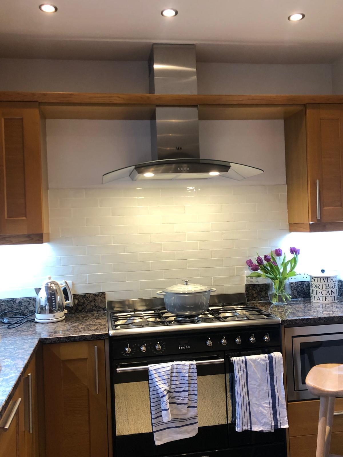 Range cooker beneath a stainless steel extractor hood with cream metro-style wall tiles